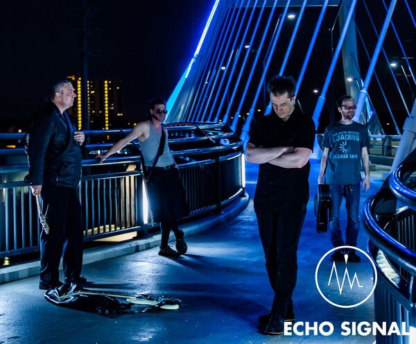 John, Phaedrus, Adam, and Charles (Echo Signal in 2016) spread along the Lowry Avenue bridge walkway at night, leaning on blue-lit railings with the lights Northeast Minneapolis behind.